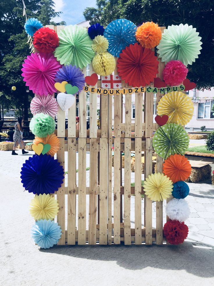 colorful paper flowers are arranged on a wooden gate for an outdoor ceremony or birthday party