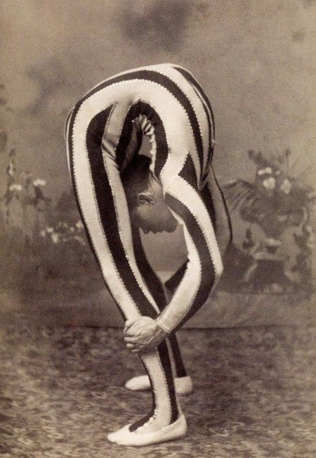 an old photo of a woman dressed in striped clothing and holding her hands behind her back