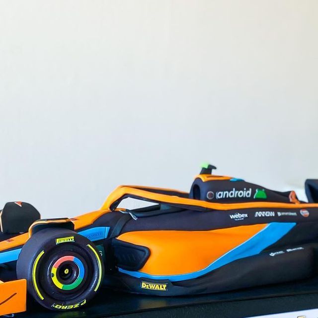 an orange and blue race car sitting on top of a black table next to a white wall