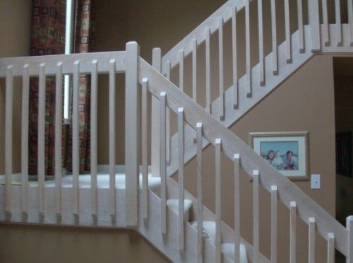 there is a white stair case in the house with pictures on the wall behind it