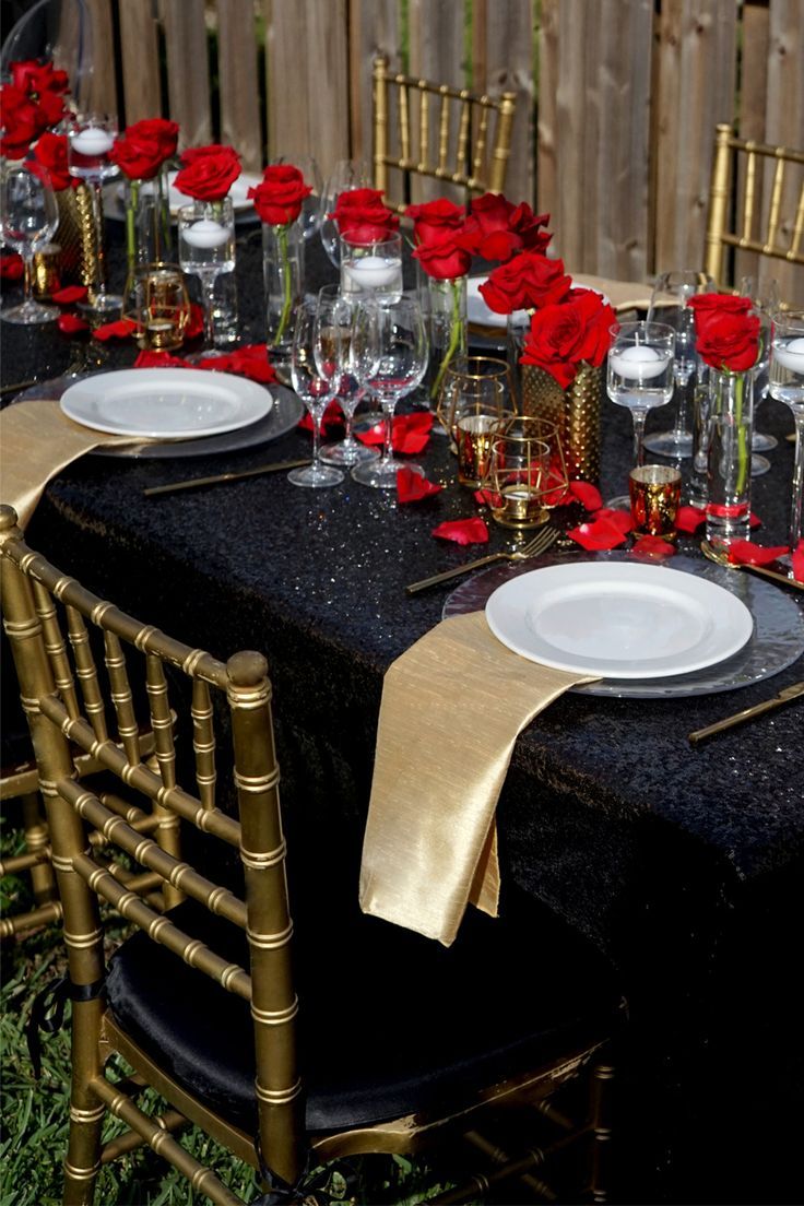 a table set with plates, silverware and red rose centerpieces on it