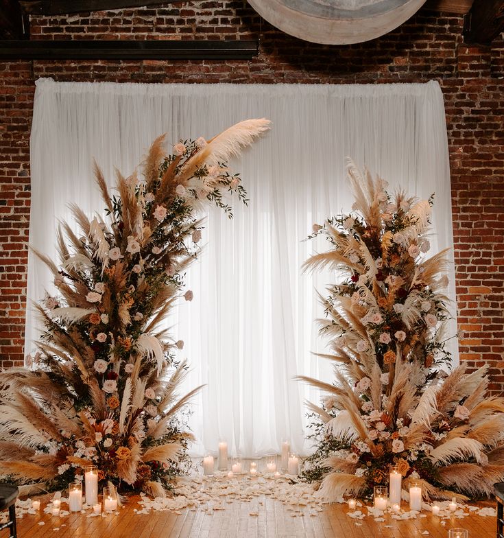 an arrangement of flowers and candles on a wooden table in front of a white curtain