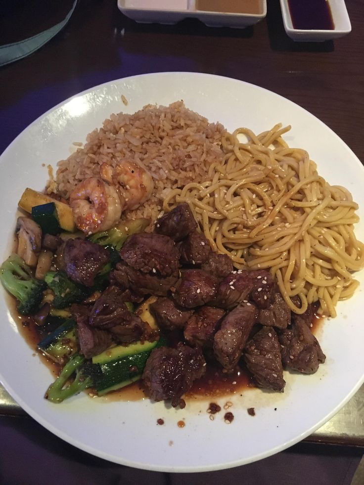 a white plate topped with meat and veggies next to noodles on a table