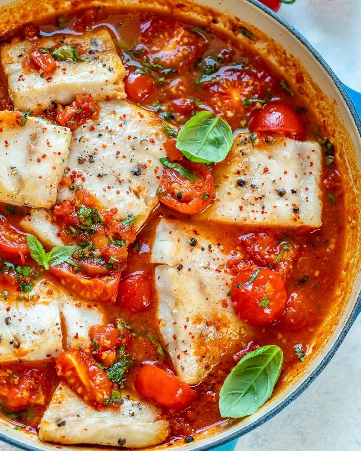 a pan filled with fish covered in tomato sauce and fresh basil garnished on top