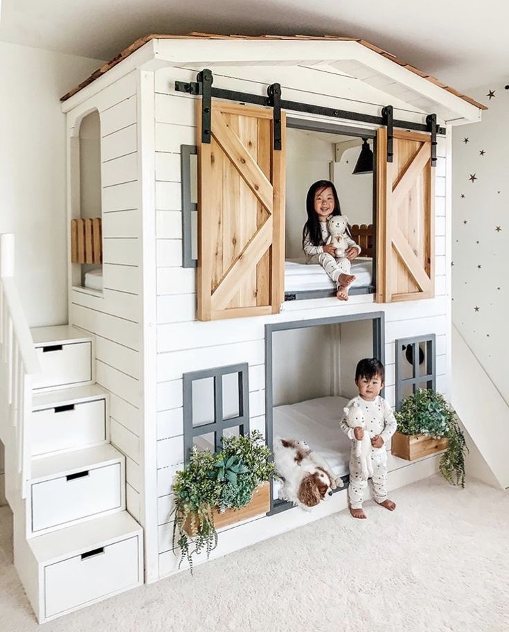 two children are sitting on the roof of a doll house with wooden doors and windows