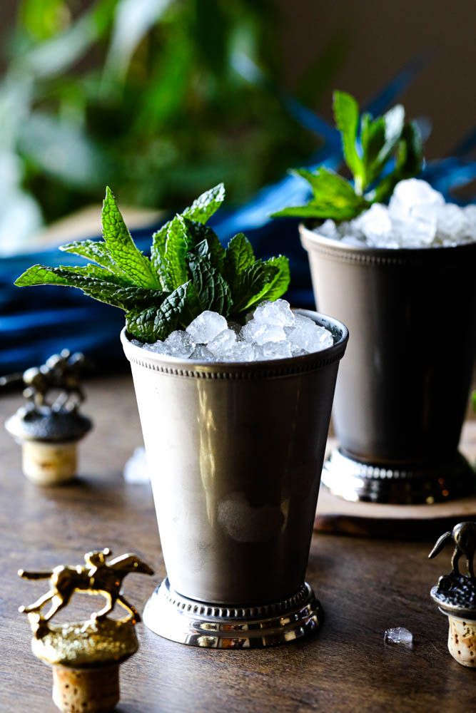 two cups filled with ice and mint sitting on top of a wooden table next to small figurines