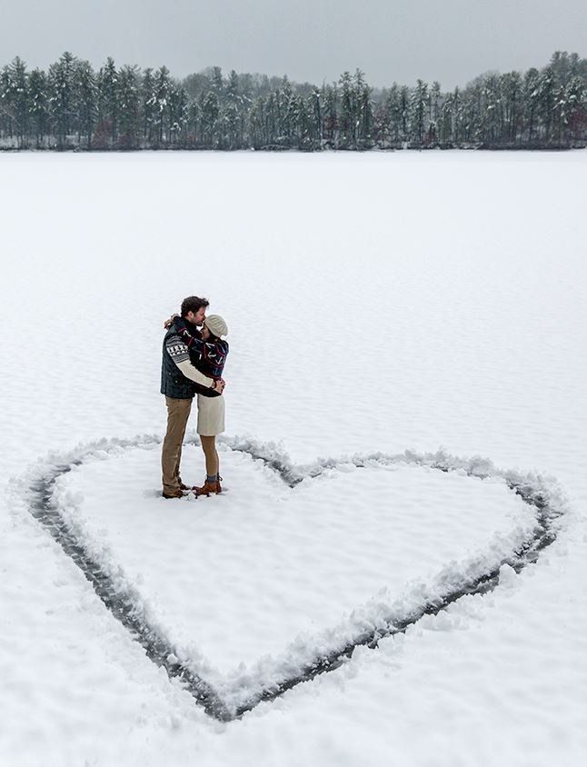 a man and woman standing in the middle of a snow covered field with a heart drawn on it