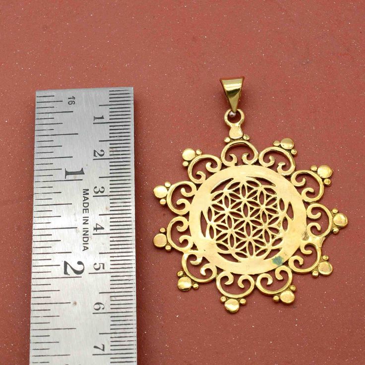 a gold plated pendant with an intricate design next to a measuring ruler on a red surface