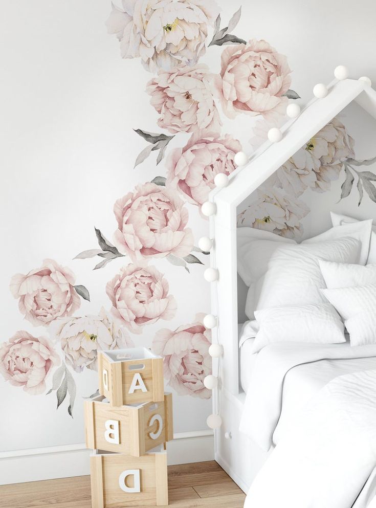 a white bedroom with pink flowers painted on the wall and wooden blocks in front of it