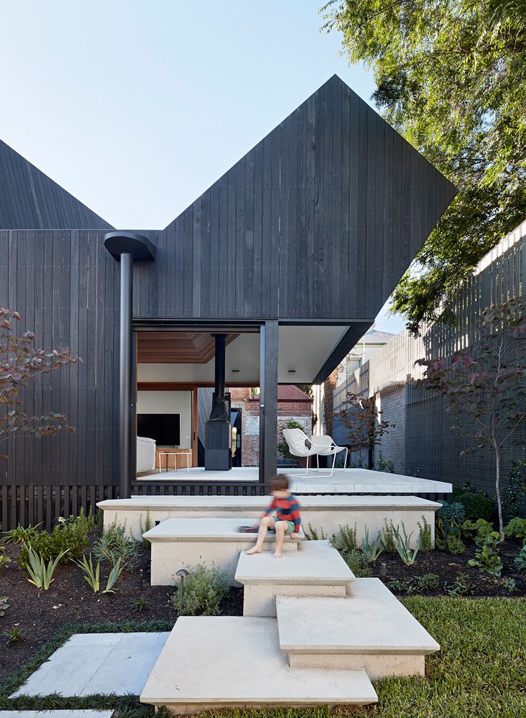 the modern house has an angled roof and is surrounded by greenery, with concrete steps leading up to the front door