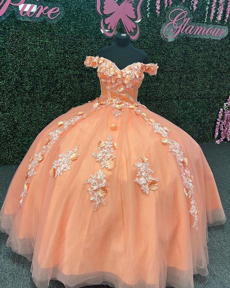 an orange ball gown on display in front of a wall with pink and white flowers