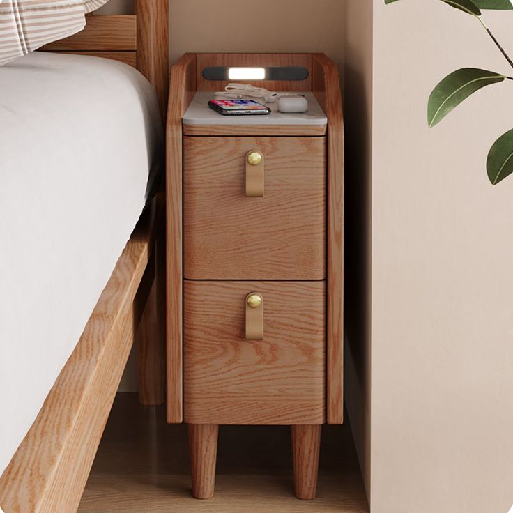 a wooden night stand next to a bed with a plant on it and a phone in the drawer