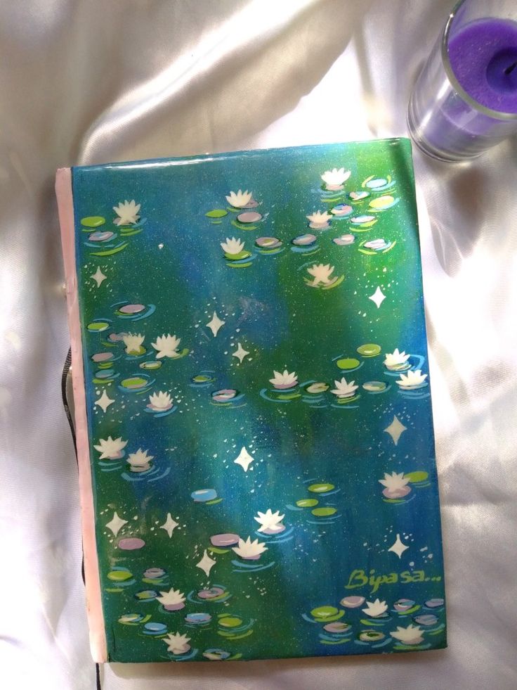 an open book with water lilies on it and a purple candle next to it