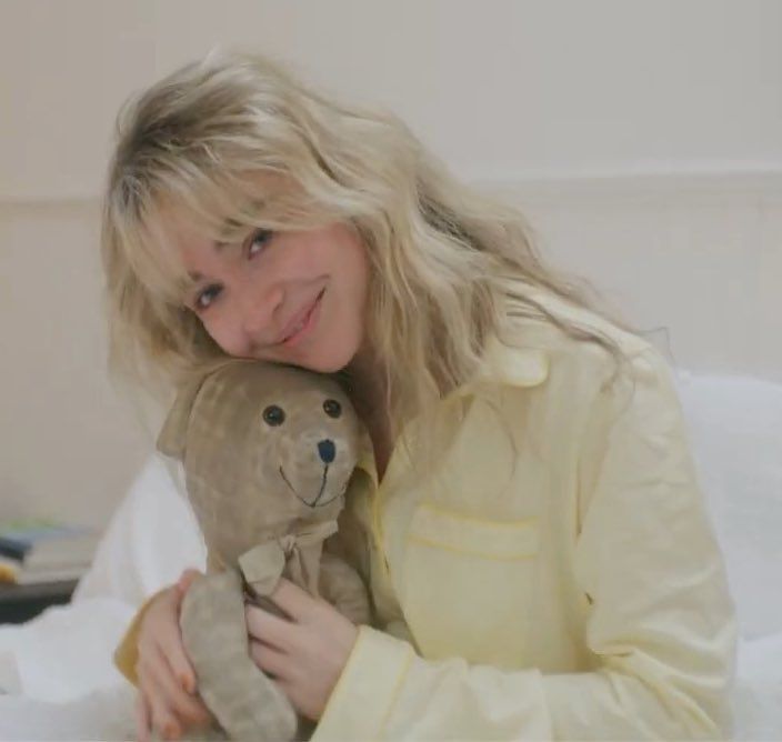 a woman is holding a teddy bear in her hands and smiling at the camera while sitting on a bed