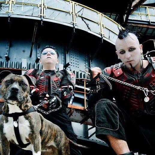 two men in black and red outfits sitting next to a dog on a leash with chains around his neck