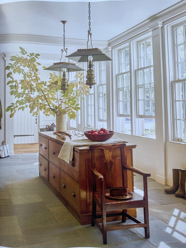 an old fashioned kitchen with a bowl of fruit on the counter and two lamps hanging from the ceiling