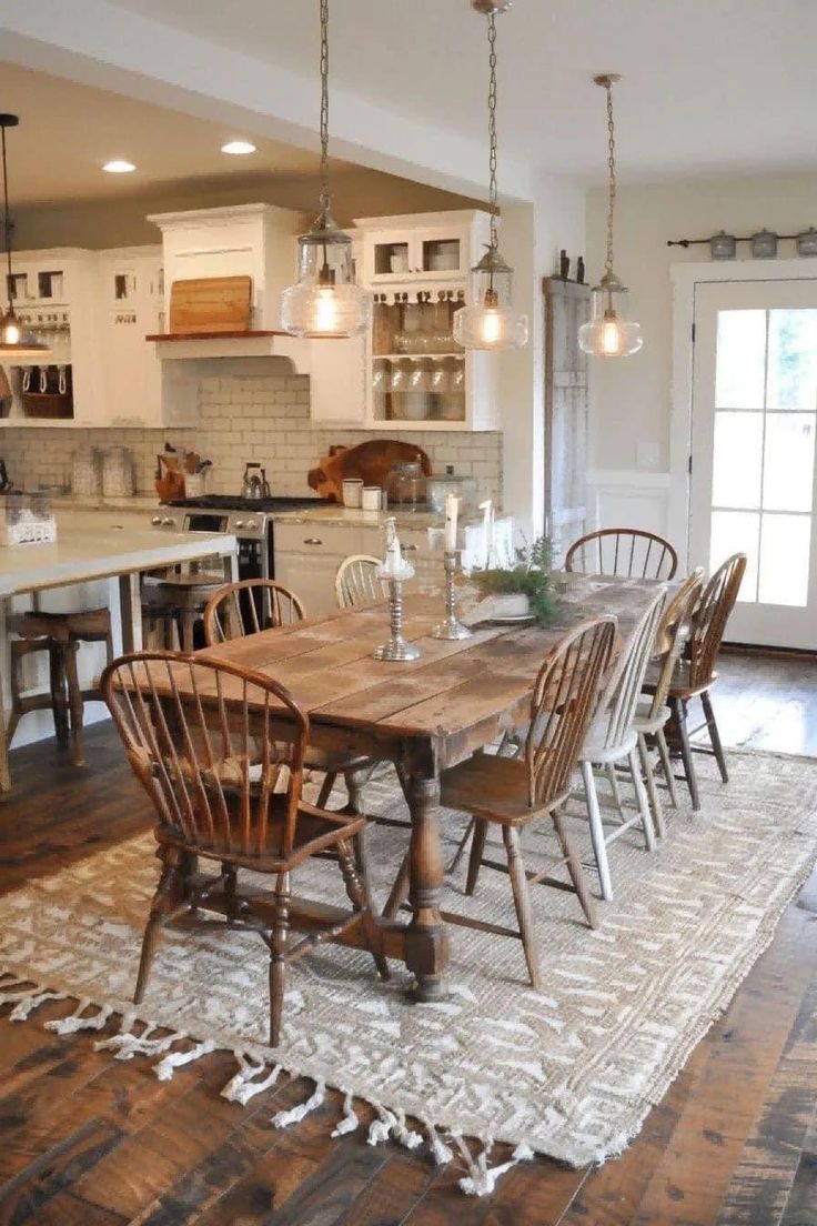 a dining room table with chairs and lights hanging from it's ceiling in front of an open kitchen