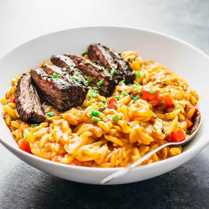 a white bowl filled with meat and rice on top of a table next to a fork