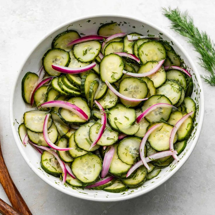 a white bowl filled with sliced cucumbers and onions next to two cinnamon sticks