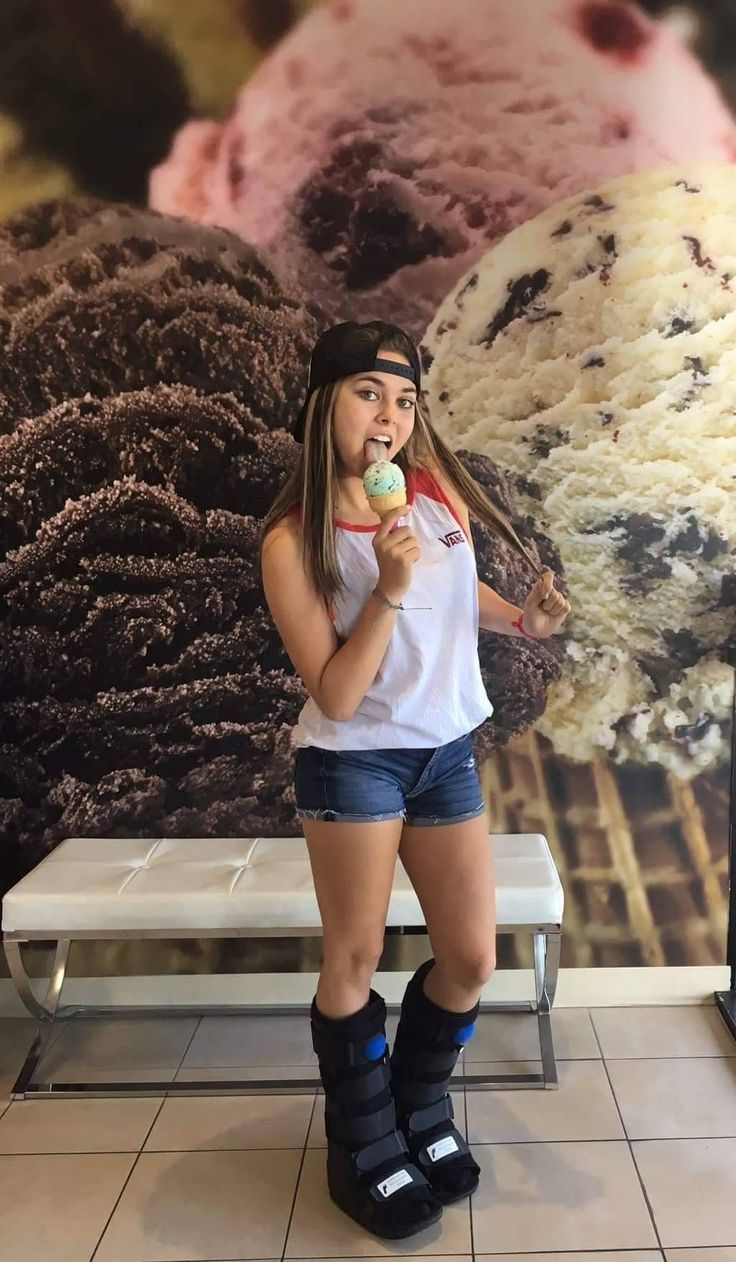 a woman is standing in front of a giant ice cream poster eating an ice cream cone