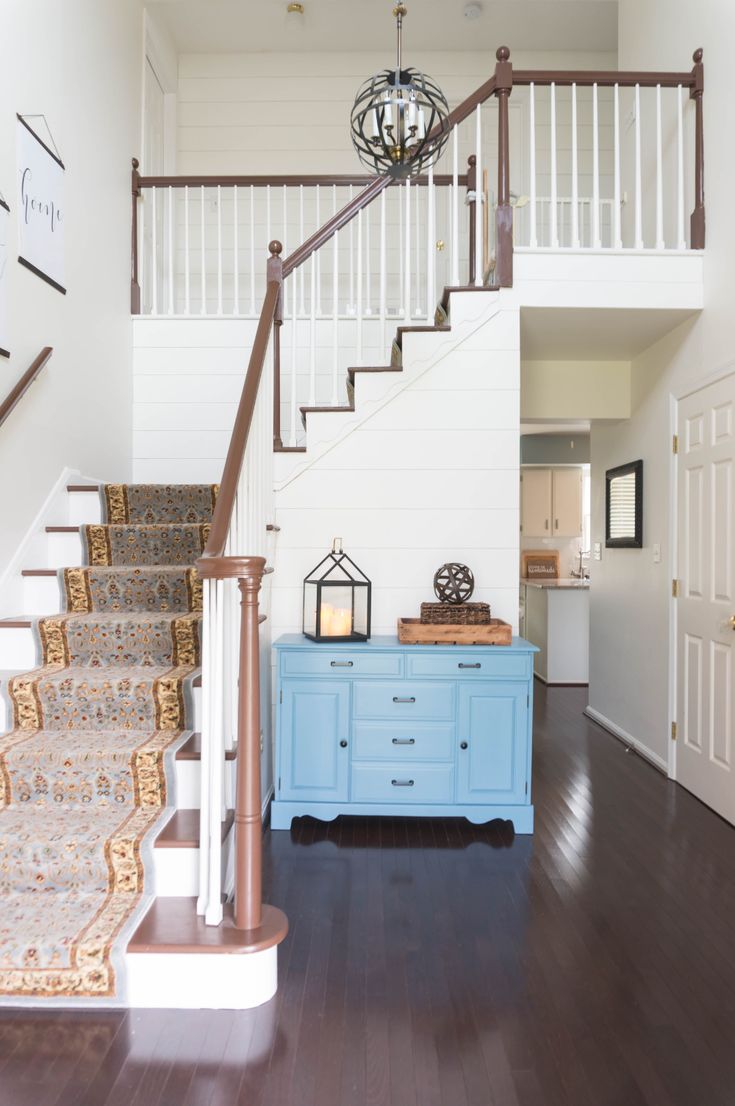 a blue dresser sitting in the middle of a hallway next to a stair case and white walls