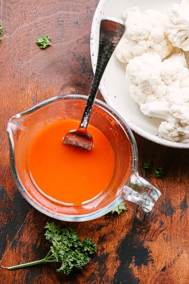 cauliflower and carrots in a bowl next to a spoon on a wooden table