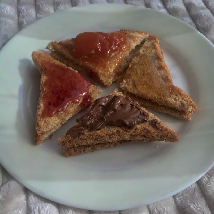 three pieces of toast with peanut butter and jelly on them sitting on a white plate