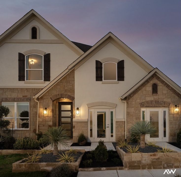 a large house with lots of windows and plants in the front yard at night time