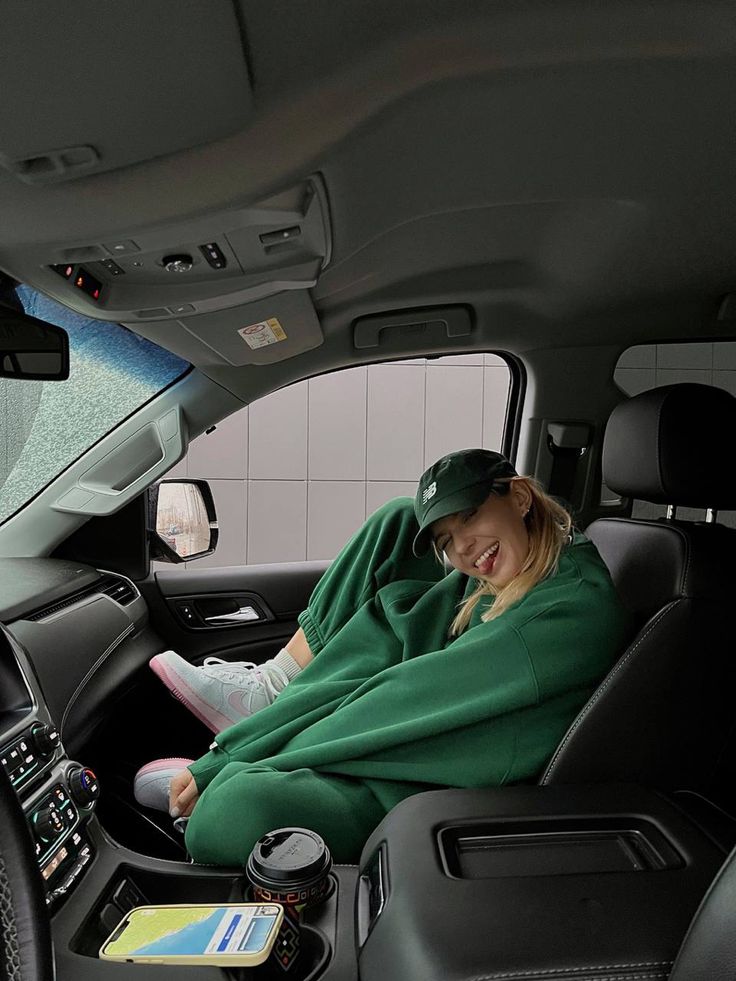 a woman sitting in the passenger seat of a car wearing a green coat and hat