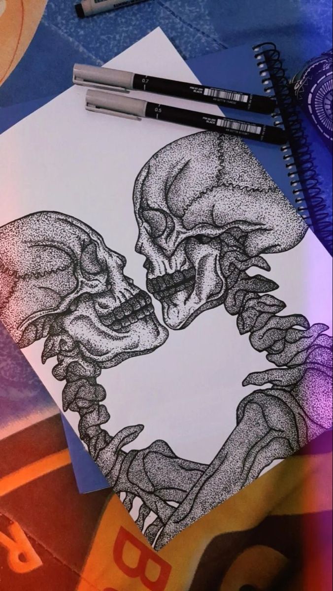 a drawing of two skulls kissing each other on top of papers with markers and pencils