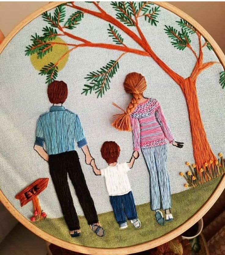 an embroidered picture of two people and a child holding hands, with a tree in the background