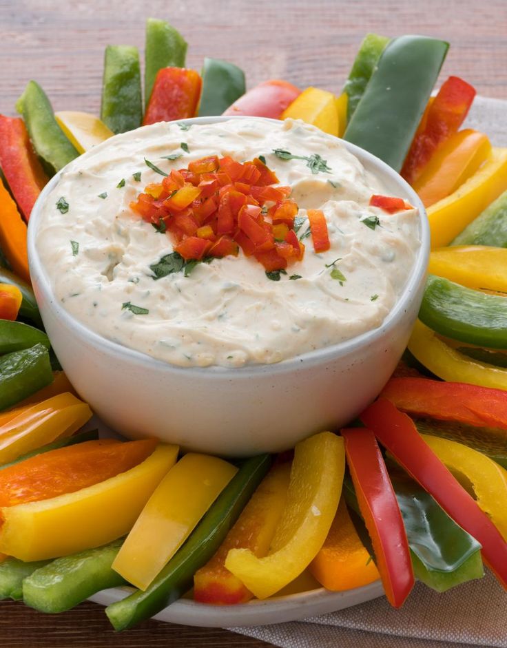 a white bowl filled with dip surrounded by veggies on a platter that says zesty herb dip and peppers