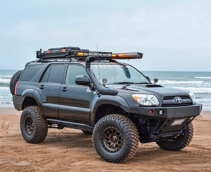 a gray four - doored suv parked on the beach with its roof rack up