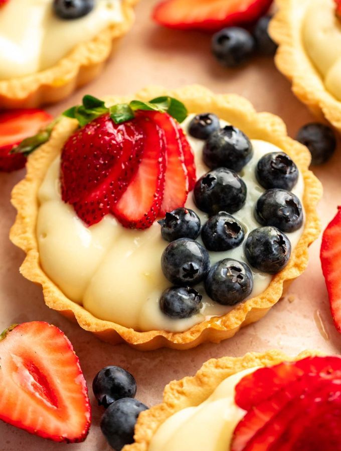 two tarts topped with berries and blueberries on top of a baking sheet next to strawberries