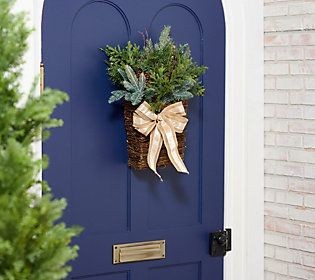 a blue front door with a basket filled with greenery and a bow hanging on it