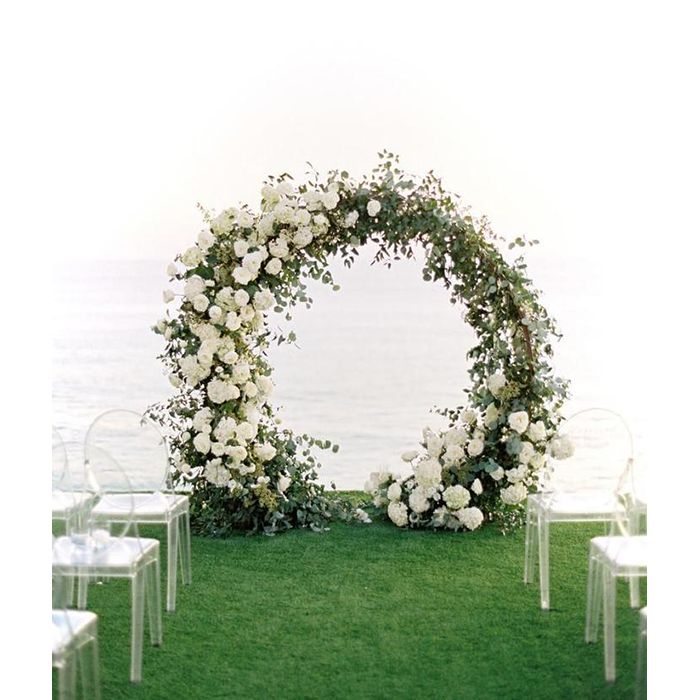 an outdoor ceremony set up with white flowers and greenery on the grass by the water