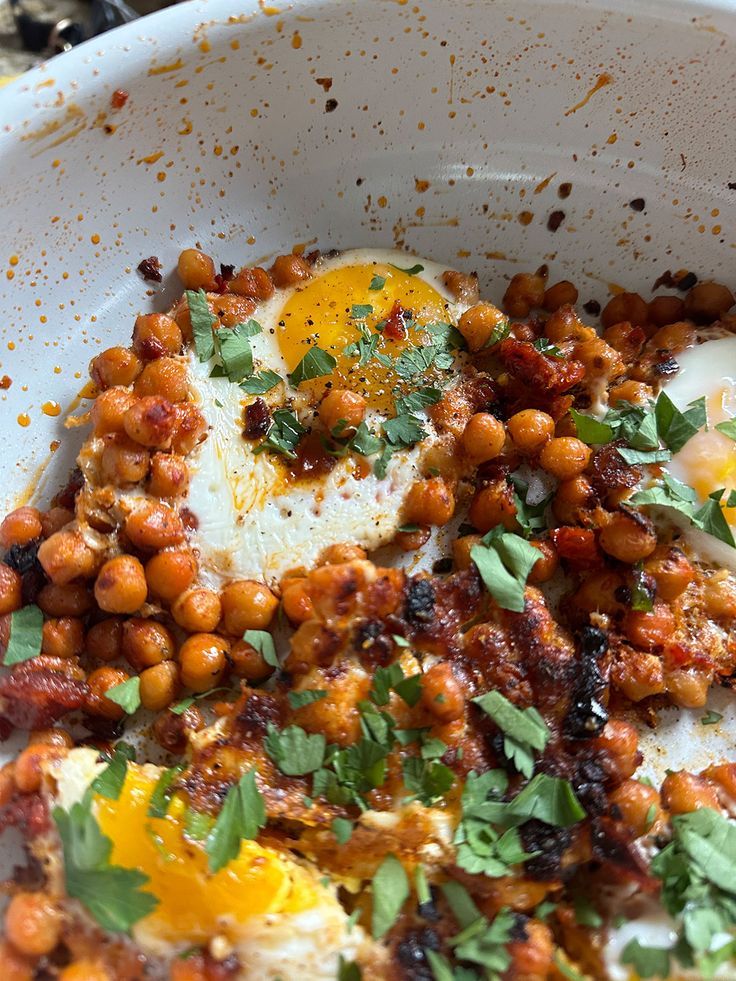 an egg is on top of chickpeas in a white bowl with parsley