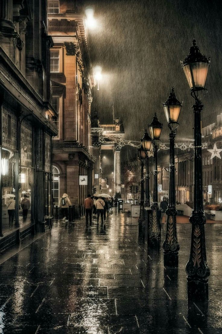 people are walking down the street in the rain at night with umbrellas and lights