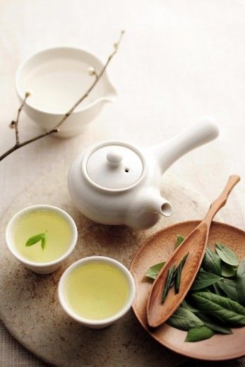 a tea pot and two cups filled with green tea sit on a plate next to some leaves