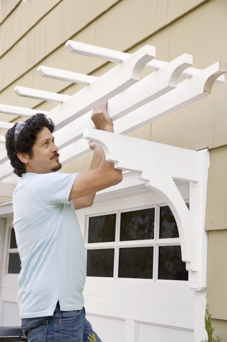 a man working on a white trellis in front of a house that is painted beige