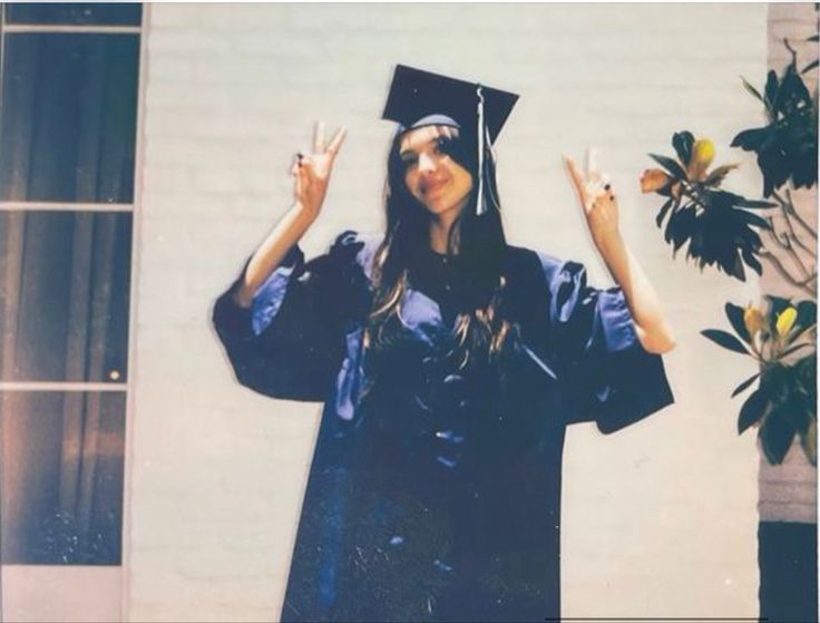 a woman wearing a graduation cap and gown holding her hands up in the air with one hand