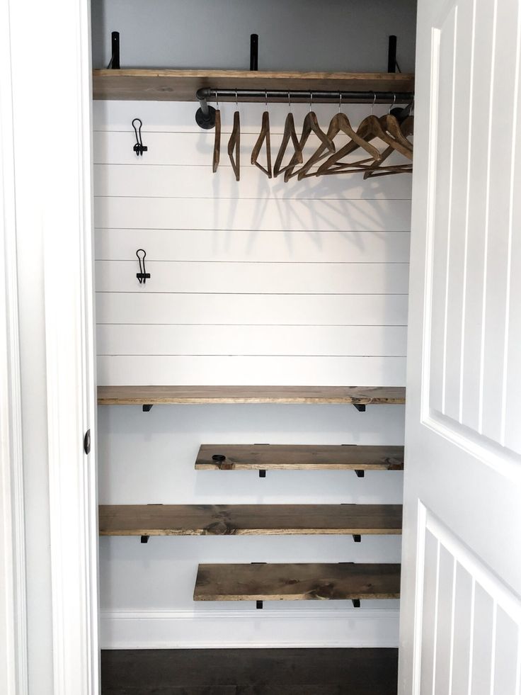 an open closet with wooden shelves and hooks on the wall, in front of white shiping