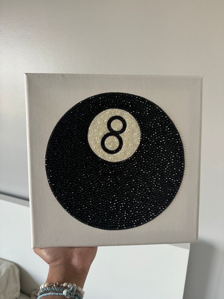 a person holding up a black and white painting with the number eight in it's center