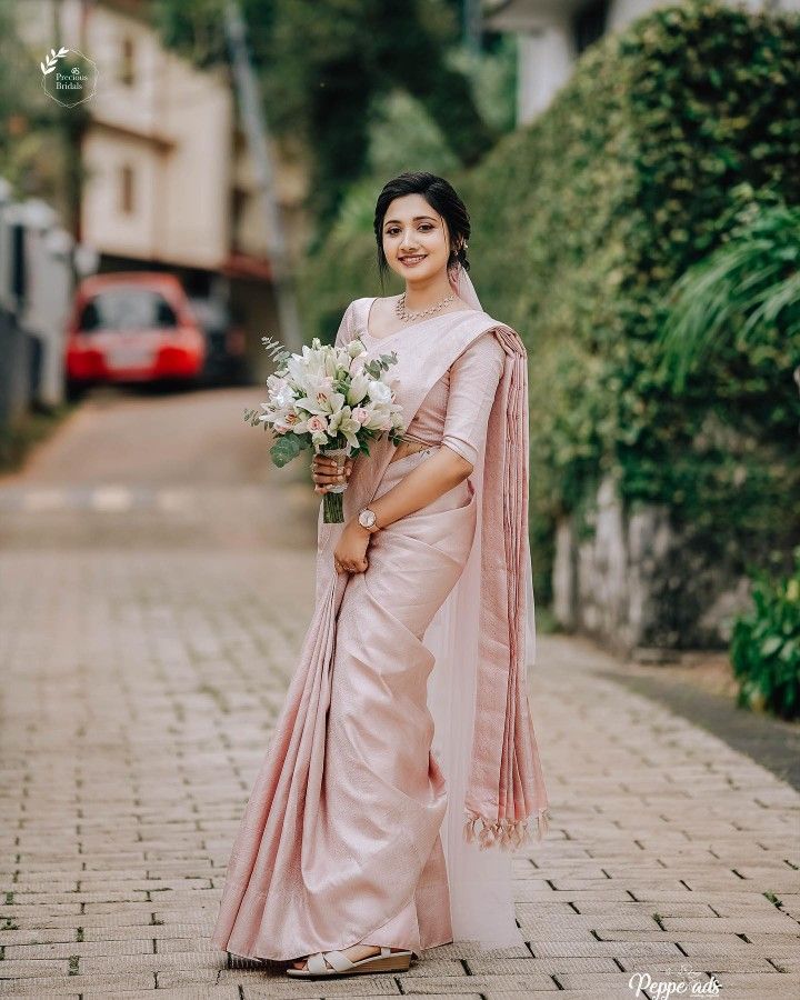 a woman in a pink sari holding a bouquet of flowers standing on a brick road