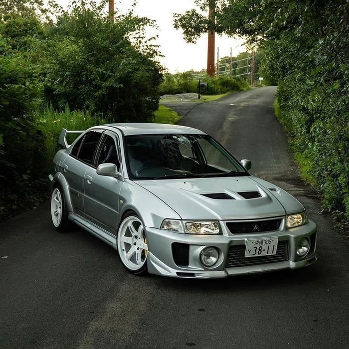 a silver car parked on the side of a road next to some bushes and trees