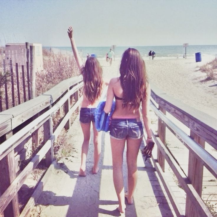 two young women walking down a boardwalk towards the beach