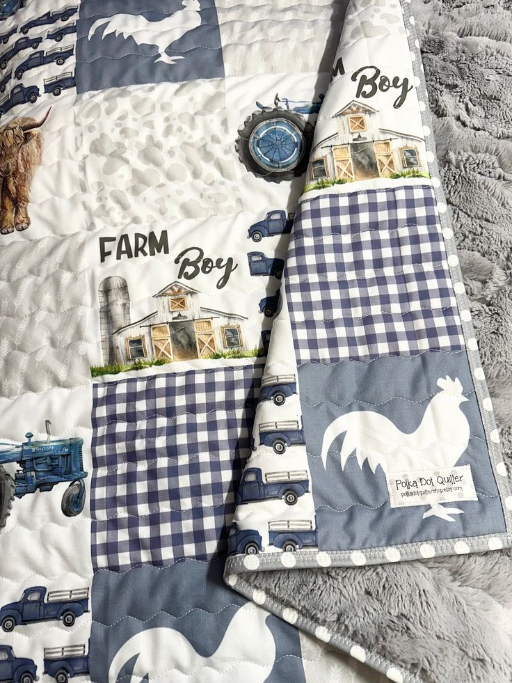 a blue and white quilt with farm animals on it's side is laying on a bed