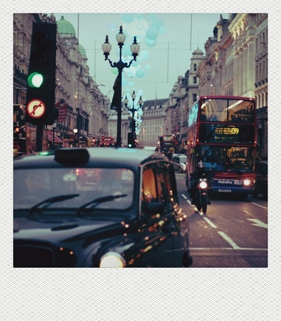 a double decker bus driving down a busy street next to traffic lights and lampsposts