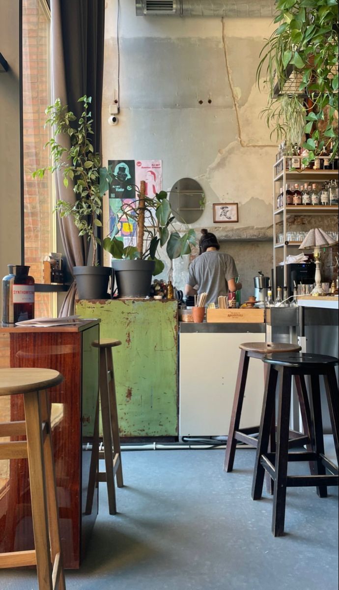 a person sitting at a counter in a room with potted plants and stools