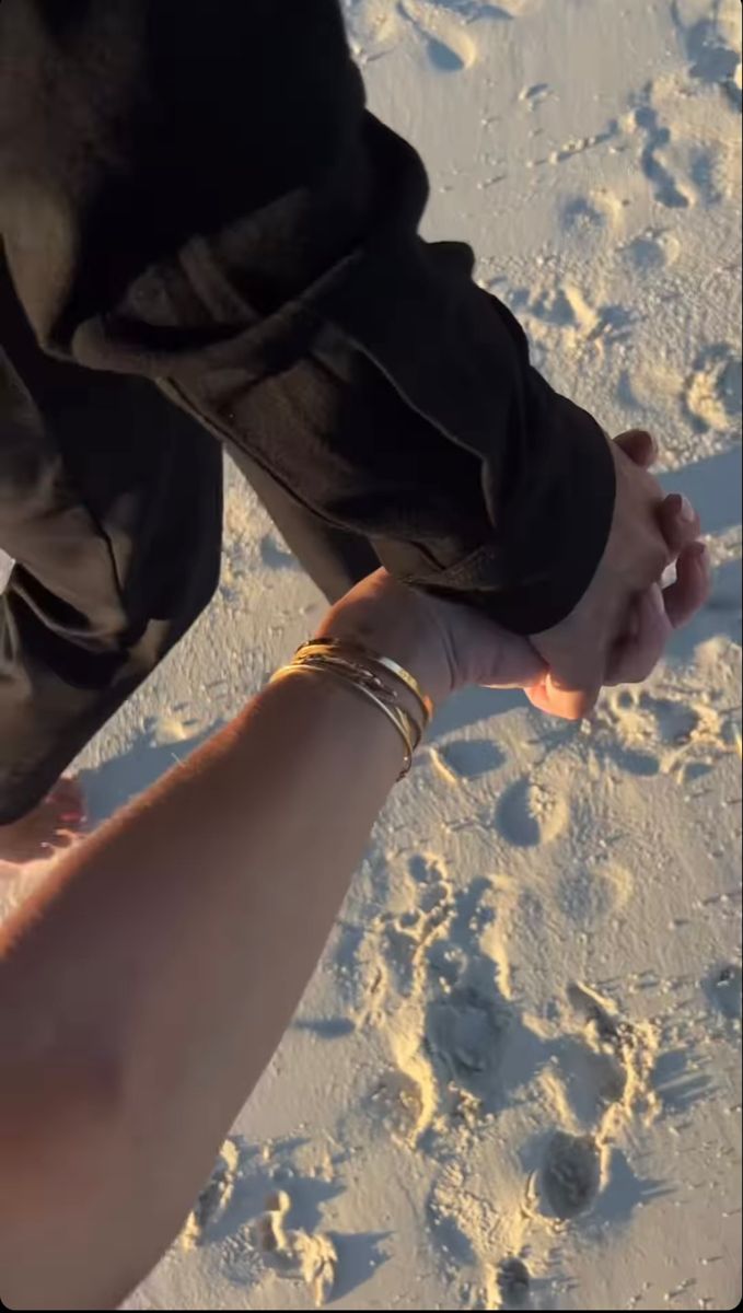 two people holding hands in the snow with footprints on the ground and one person's arm